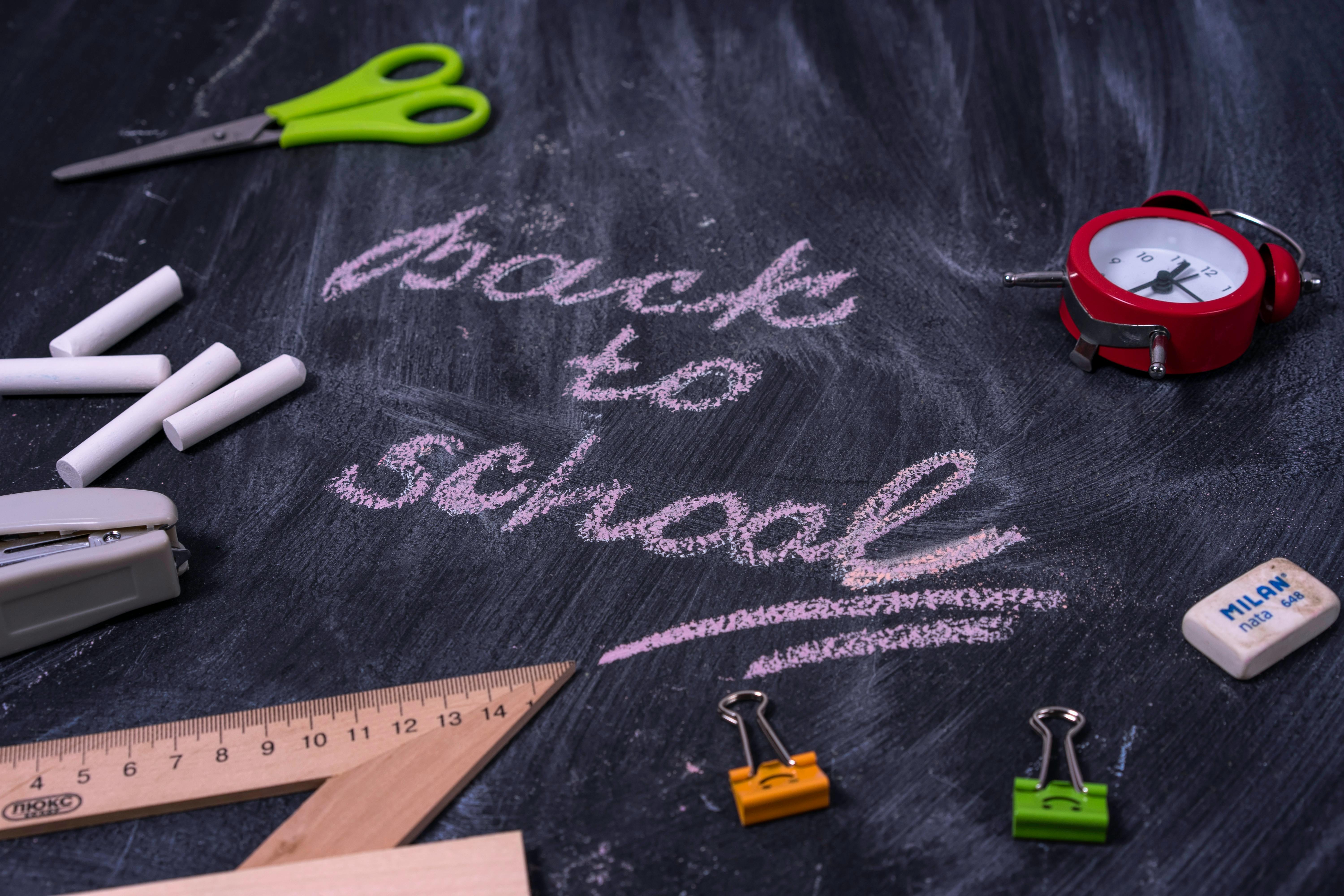 Back to school written in chalk on a classroom whiteboard with school stationery, backpacks, and supplies – start of the new school year 2025